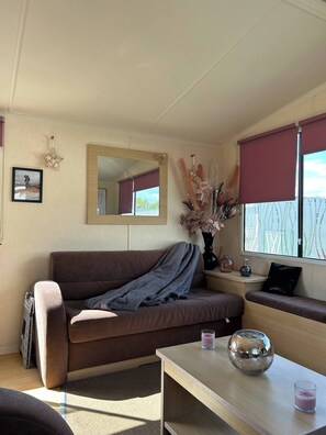 A cozy living room with a brown sofa, a wooden coffee table, and a window with a view of greenery. - Charming Holiday Park Retreat in Morecambe - Family-Friendly Escape (Morecambe)