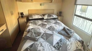 A compact bedroom with a bed, bedside tables, a headboard, and a window. - Charming Holiday Park Retreat in Morecambe - Family-Friendly Escape (Morecambe)