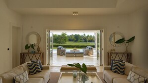 Ein geräumiges Wohnzimmer mit großem Fenster und Blick auf einen gepflegten Rasen und Bäume. In der Mitte stehen zwei Sofas und ein Couchtisch.