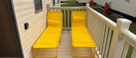 A deck with two yellow lounge chairs and a white railing.