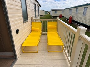 Eine Terrasse mit zwei gelben Liegestühlen und einem weißen Geländer.