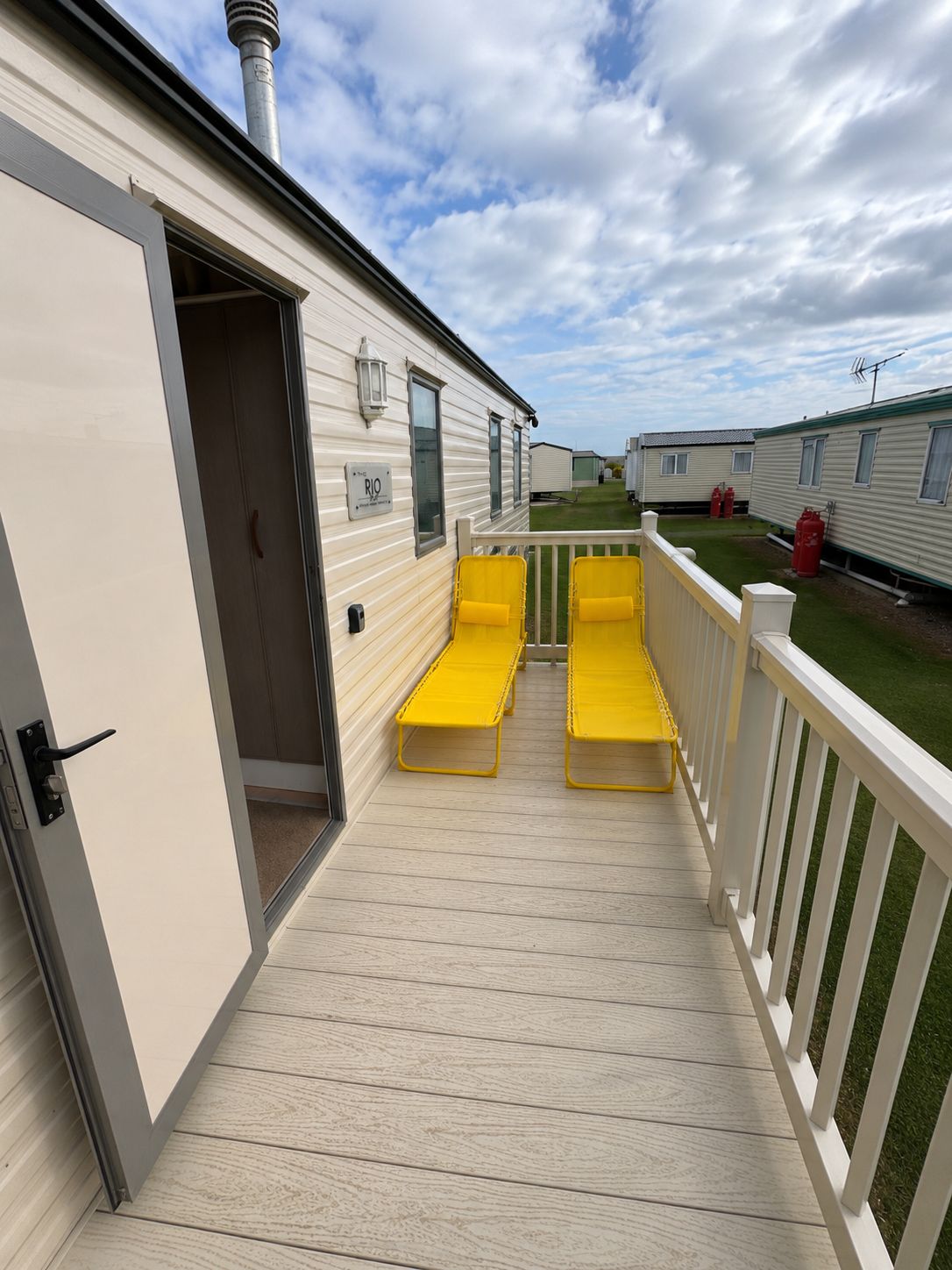 A mobile home with a deck, yellow lounge chairs, and a white fence.