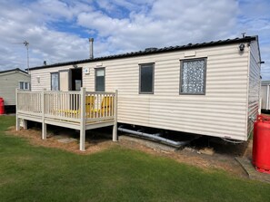 A mobile home with a deck, a chimney, and a window with a decorative screen. - Singh&Leite Family L6 (Clacton-on-Sea)