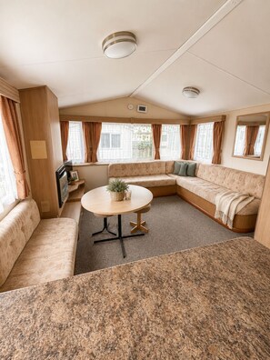 Ein gemütliches Wohnmobil-Interieur mit einer Eckcouch, einem runden Tisch und einer Küchenzeile.