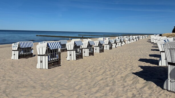 Une plage bordée de rangées de cabanes de plage blanches, surmontées d’auvents à rayures bleues.