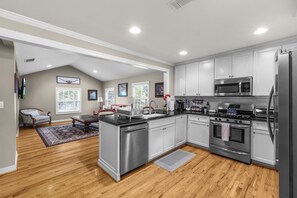 A modern kitchen with stainless steel appliances, wooden flooring, and a view of a living room with a sofa and a fireplace. - Cozy home in Ft Worth, walk to Dickies Arena & Will Rogers Coliseum horse show (Fort Worth)