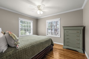 A bedroom with a bed, two windows with blinds, a ceiling fan, and a dresser.