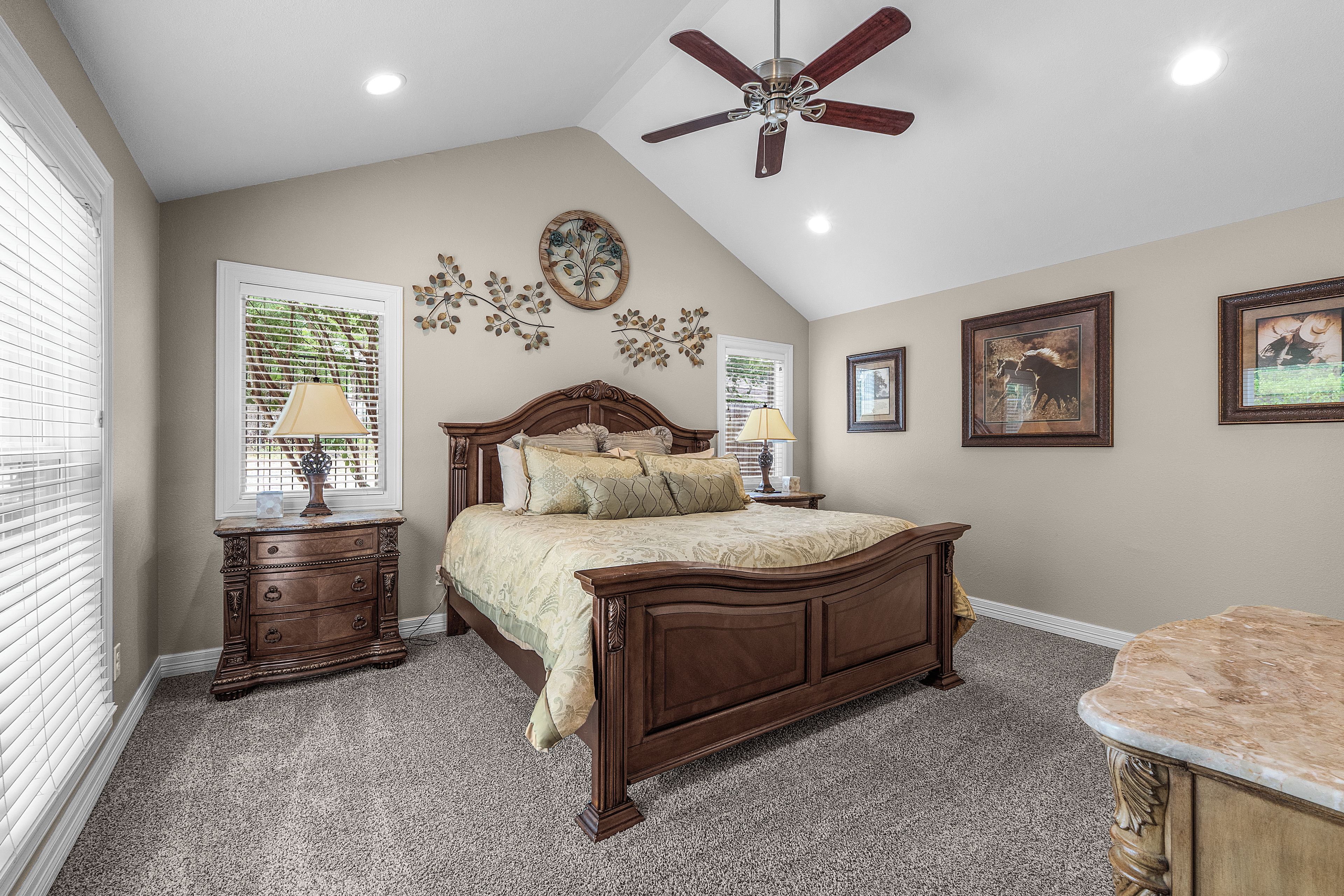 A bedroom with a large bed, two bedside tables, a ceiling fan, and wall decorations.