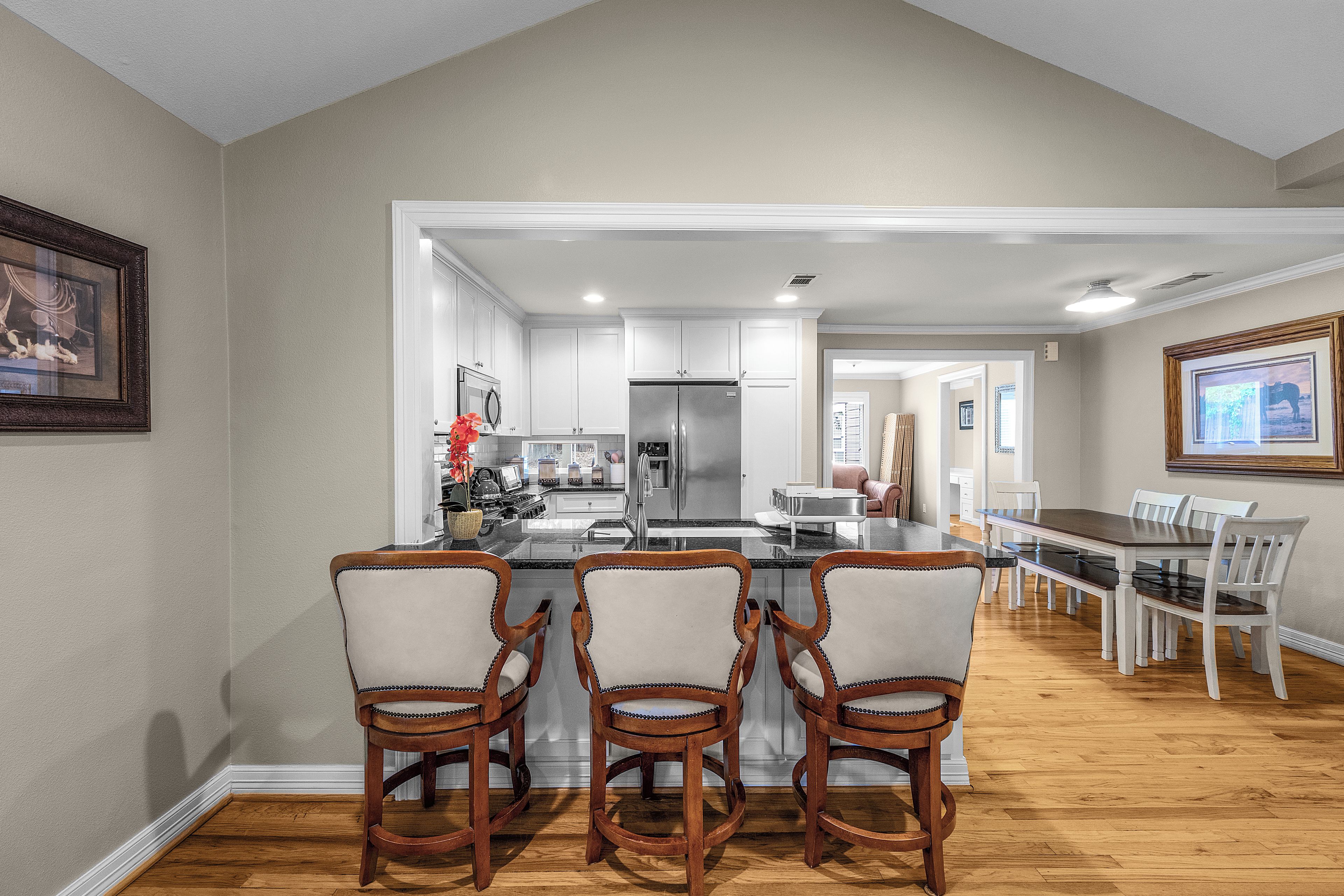 A modern kitchen with white cabinetry, a stainless steel refrigerator, and a bar area with wooden chairs.