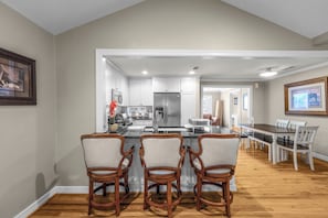 A modern kitchen with white cabinetry, a stainless steel refrigerator, and a bar area with wooden chairs.