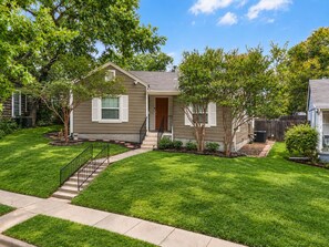 A residential house with a front yard, a staircase leading to the entrance, and a small tree.