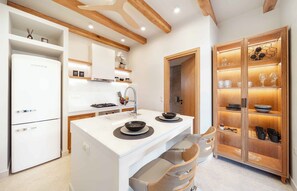 A modern kitchen with white cabinetry, a built-in island, wooden beams, and a glass-fronted cabinet with dishes. - SunKeramos Retreat -Free*Heated Pool Private Villa (Phylaki)