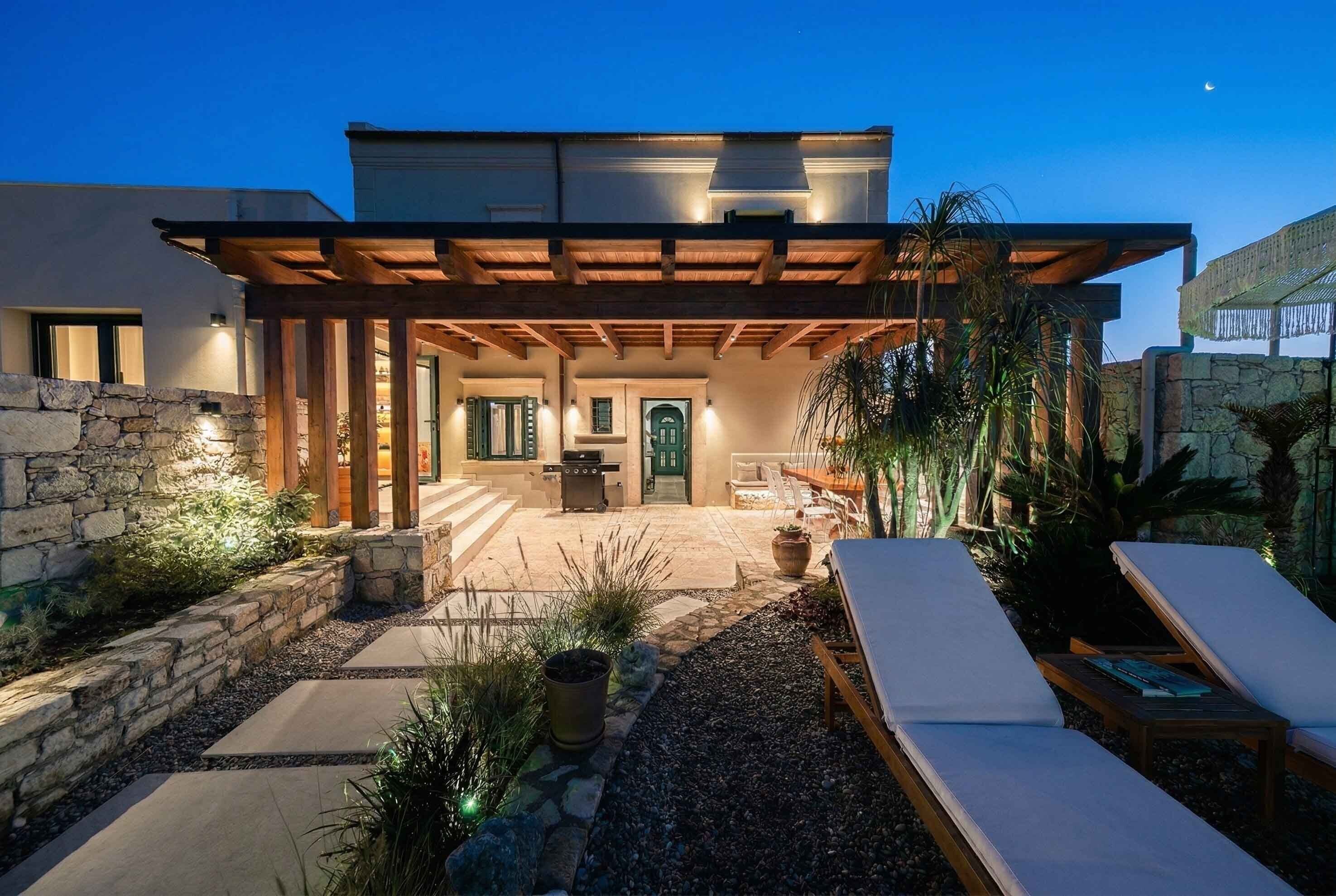 Una casa moderna con un porche cubierto, muros de piedra y mobiliario para exterior.