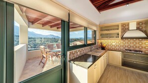 A kitchen with a view of the countryside, a balcony with a table and chairs, and patterned tiles on the backsplash. - SunKeramos Retreat -Free*Heated Pool Private Villa (Phylaki)