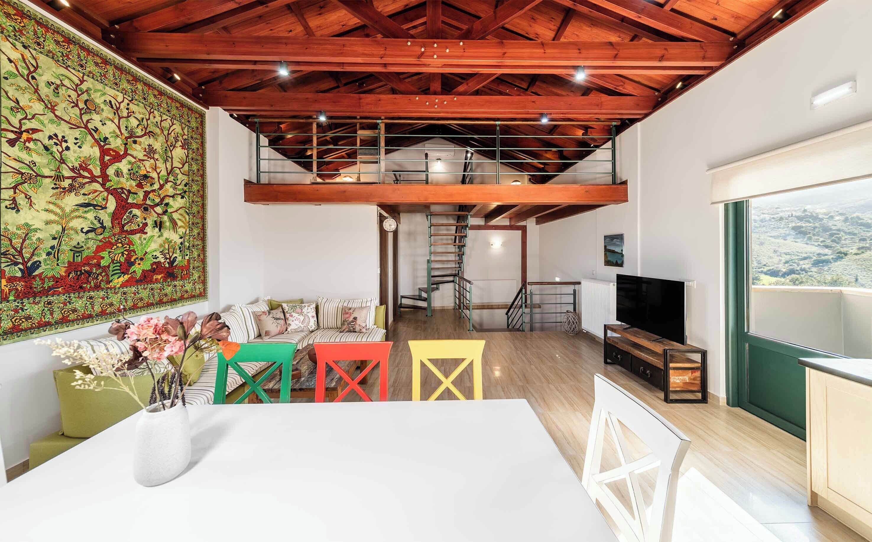 Een ruime loft met een hoge plafond, een wenteltrap, een grote tv en uitzicht op het landschap.