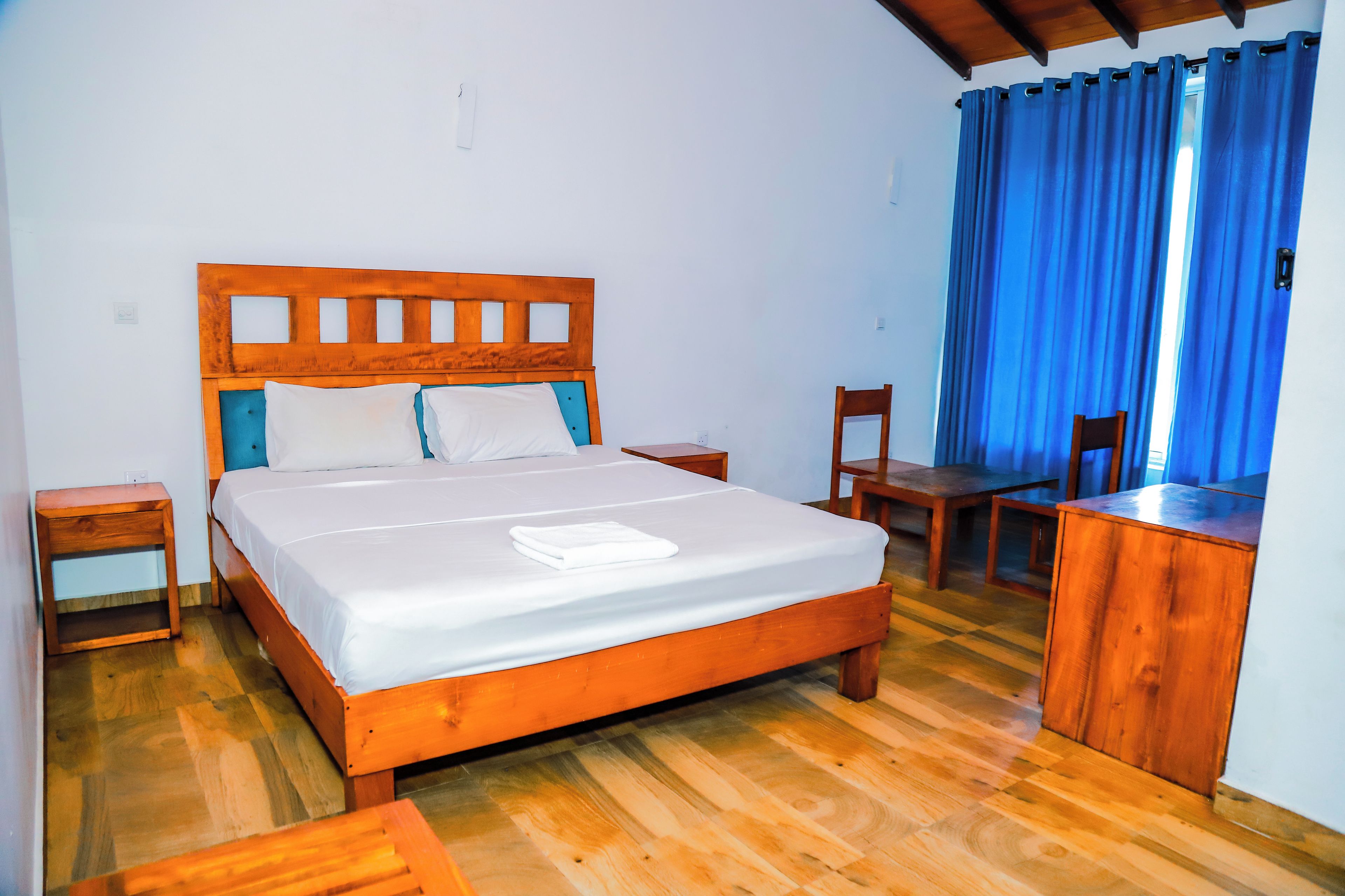 A wooden bed with white linens, a wooden nightstand, a wooden desk, and a chair.