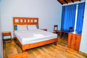 Una cama de madera con ropa de cama blanca, una mesita de noche de madera, un escritorio de madera y una silla.