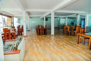 Un espacio interior amplio con varias mesas y sillas de madera, piso con diseño y divisiones de vidrio.