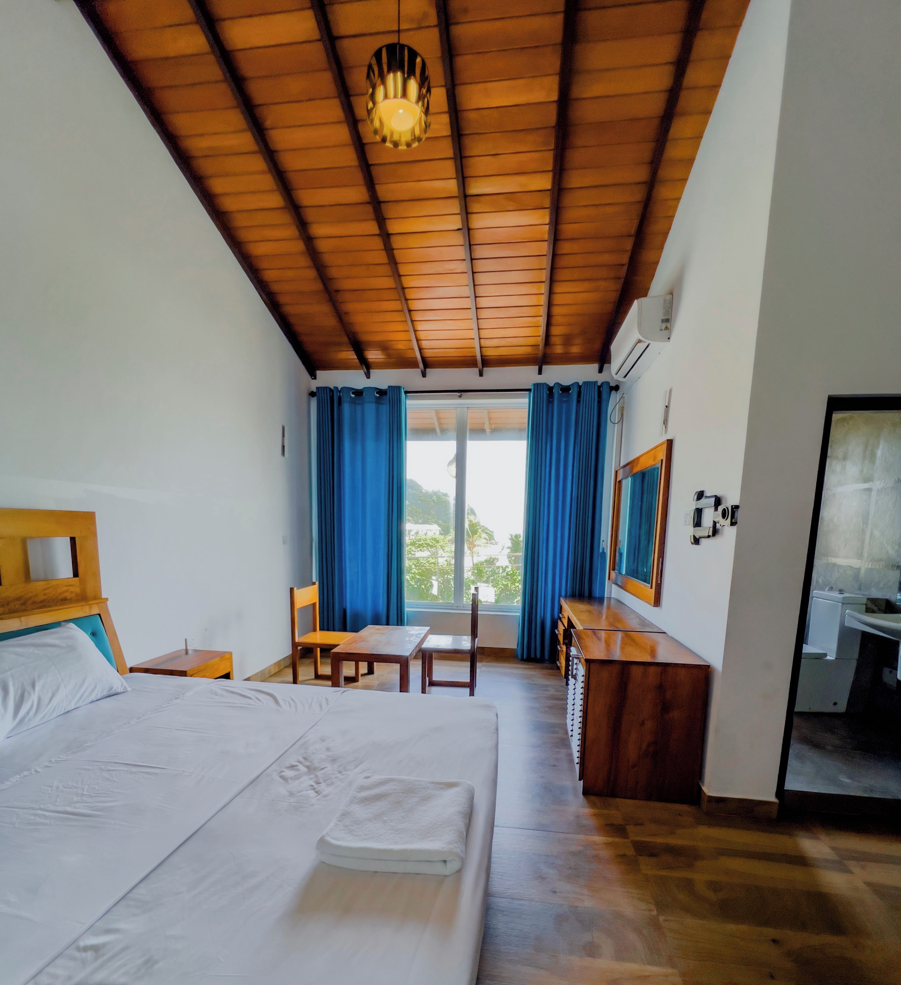 A hotel room with a bed, a desk, a chair, a window with curtains, and a ceiling fan.