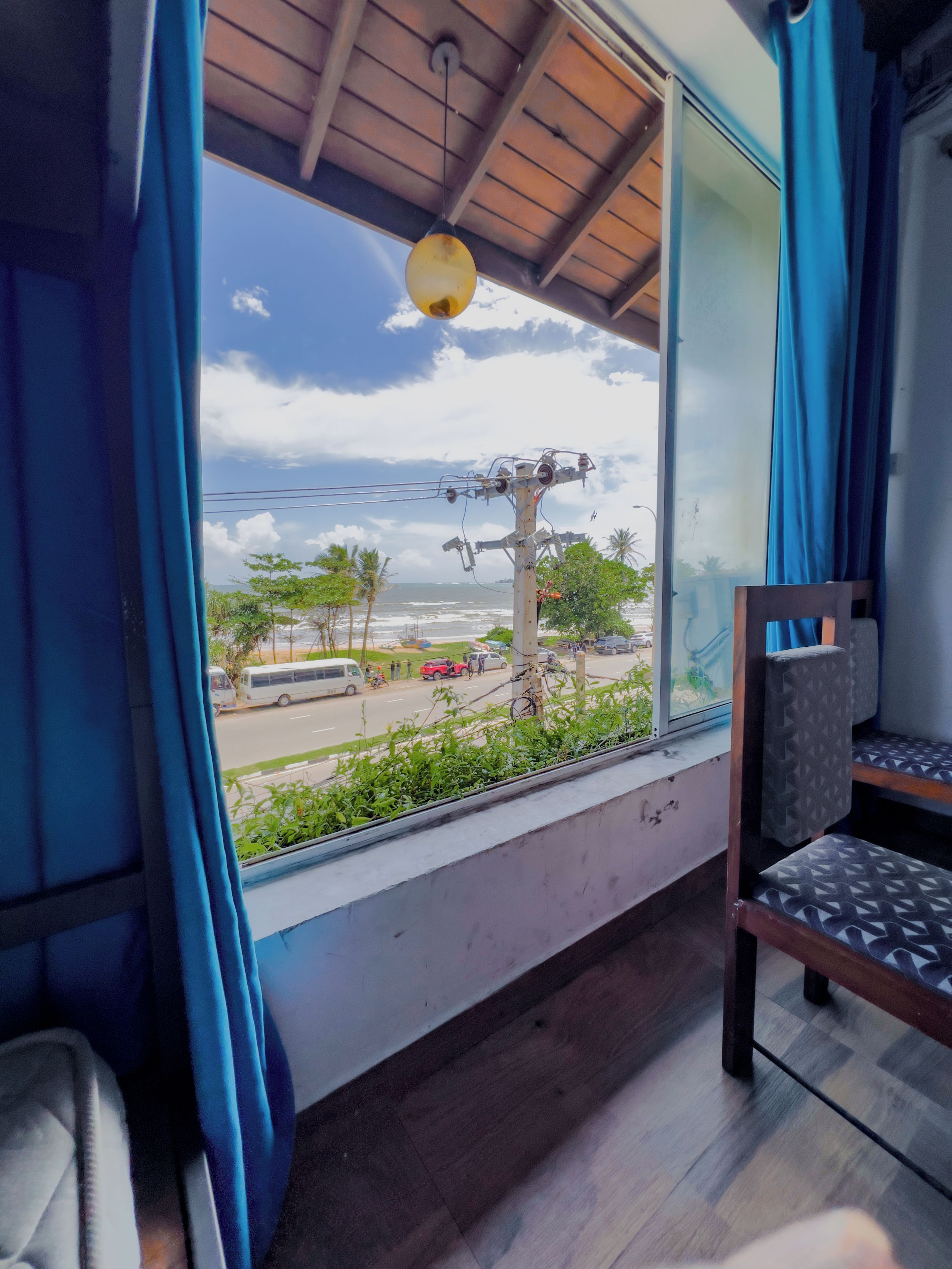 Una habitación con ventana que da a la calle, una silla y una estructura de líneas eléctricas en el exterior.