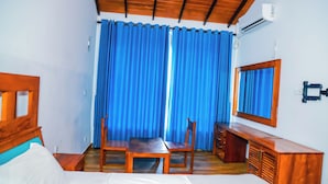 Habitación de hotel con cama, un escritorio de madera, una silla, un espejo y una ventana con cortinas azules.