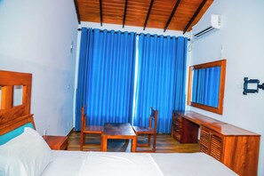 Habitación de hotel con cama, un escritorio de madera, una silla, un espejo y una ventana con cortinas azules.