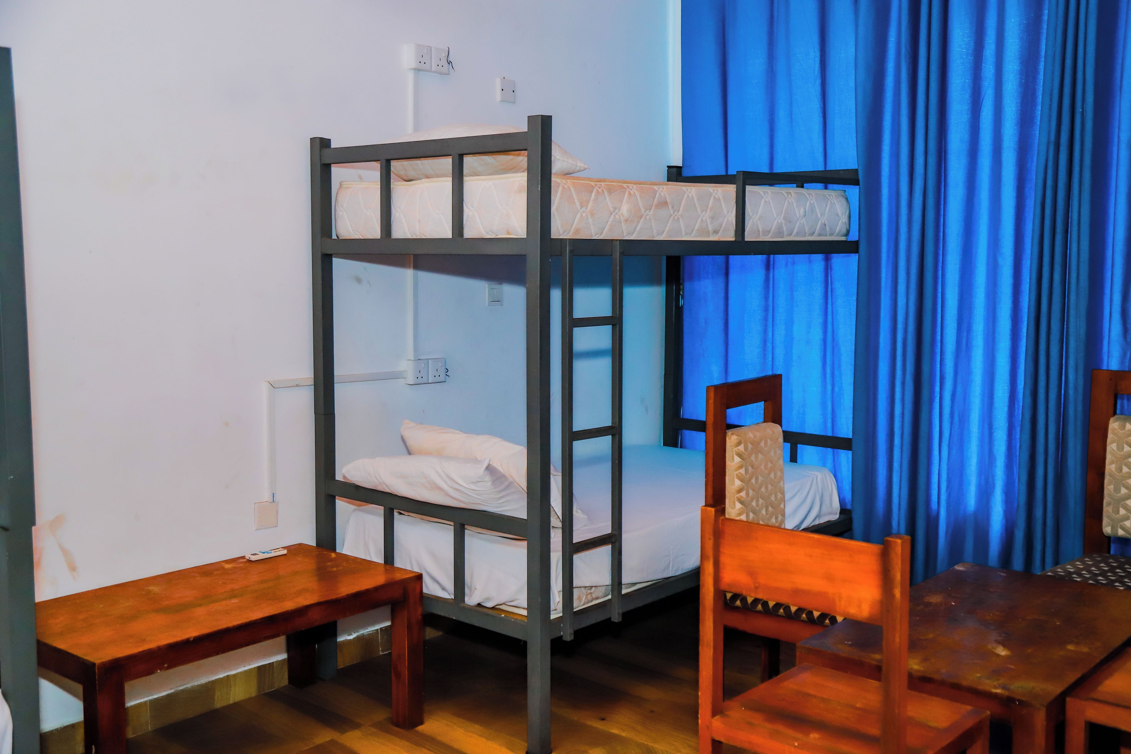 Una cama litera con escalera, una mesa de madera y una silla en una habitación con cortinas azules.