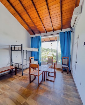 Habitación con literas, una mesa, sillas y vista a través de una ventana con cortinas.