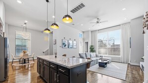 A spacious kitchen with a central island, wooden flooring, pendant lighting, and a ceiling fan. - Luxury 3Bed/3.5Bath Townhome 10 Minutes from Downtown HTX (Houston)
