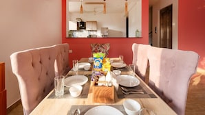 Un coin repas avec une table dressée pour quatre personnes, deux chaises rembourrées, une cuisine en arrière-plan et un mur d’accent de couleur rouge.