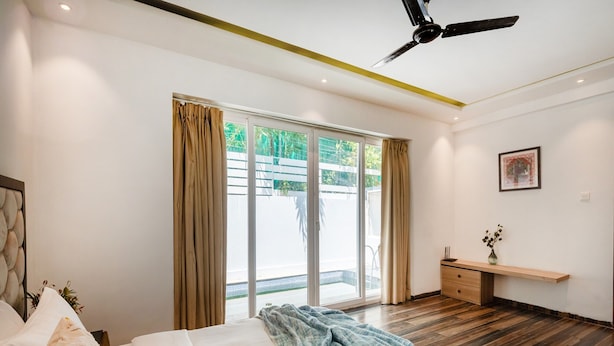 Une chambre moderne avec un lit, un ventilateur de plafond, une porte-fenêtre coulissante et un petit bureau agrémenté d’un vase.