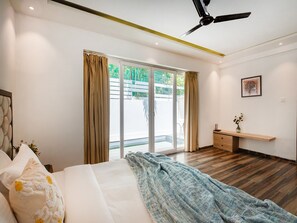 A modern bedroom with a bed, a ceiling fan, a sliding glass door, and a small desk with a vase.