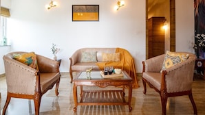 Un salon comprenant un canapé, deux fauteuils, une table basse et des coussins décoratifs. On y trouve également des appliques murales et une œuvre d’art encadrée au-dessus du canapé.