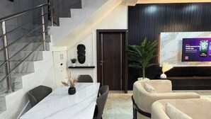 Ein moderner Wohnbereich mit Esstisch, Stühlen, einer Couch, einem Fernseher und einer Treppe.