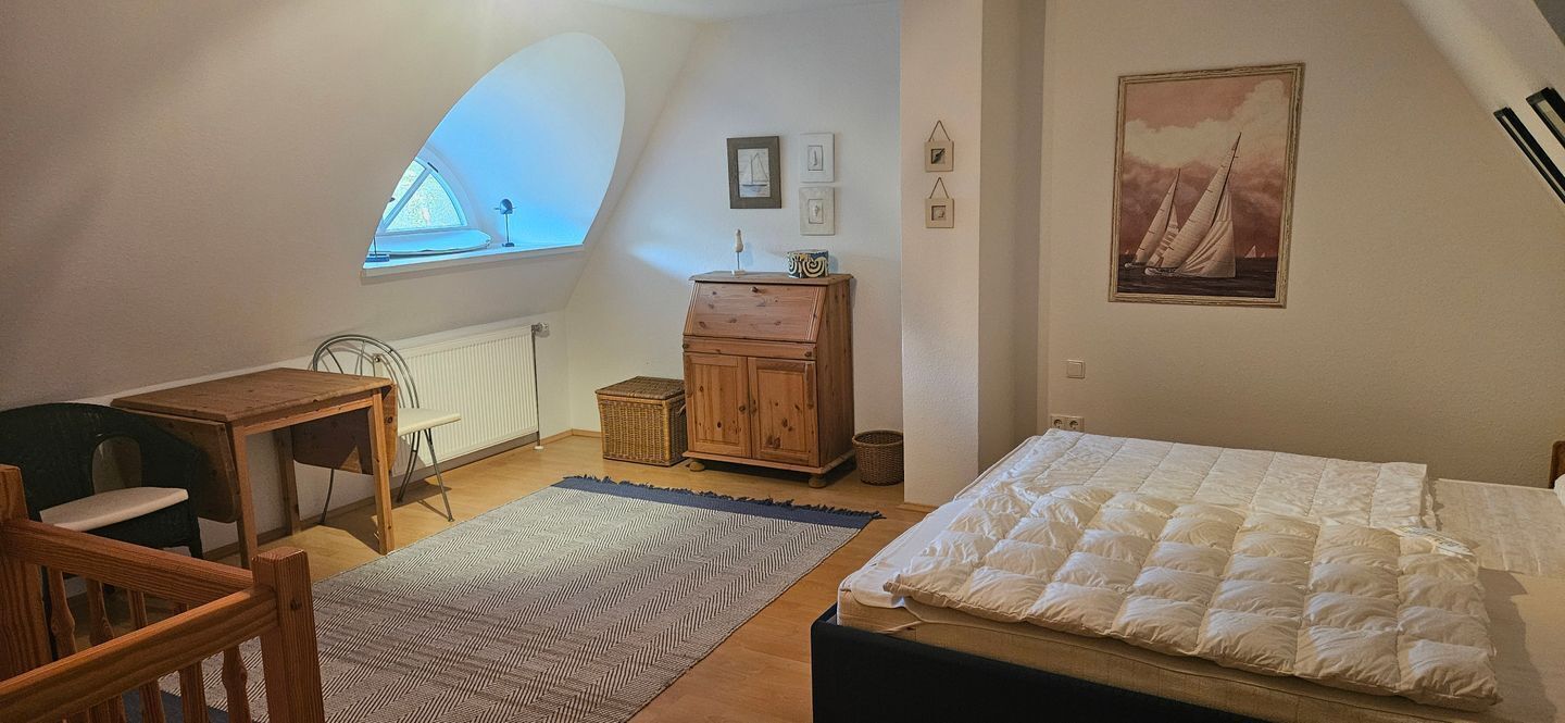 Ett mysigt sovrum med en säng, ett skrivbord och en stol, ett fönster med utsikt och en tavla på väggen.