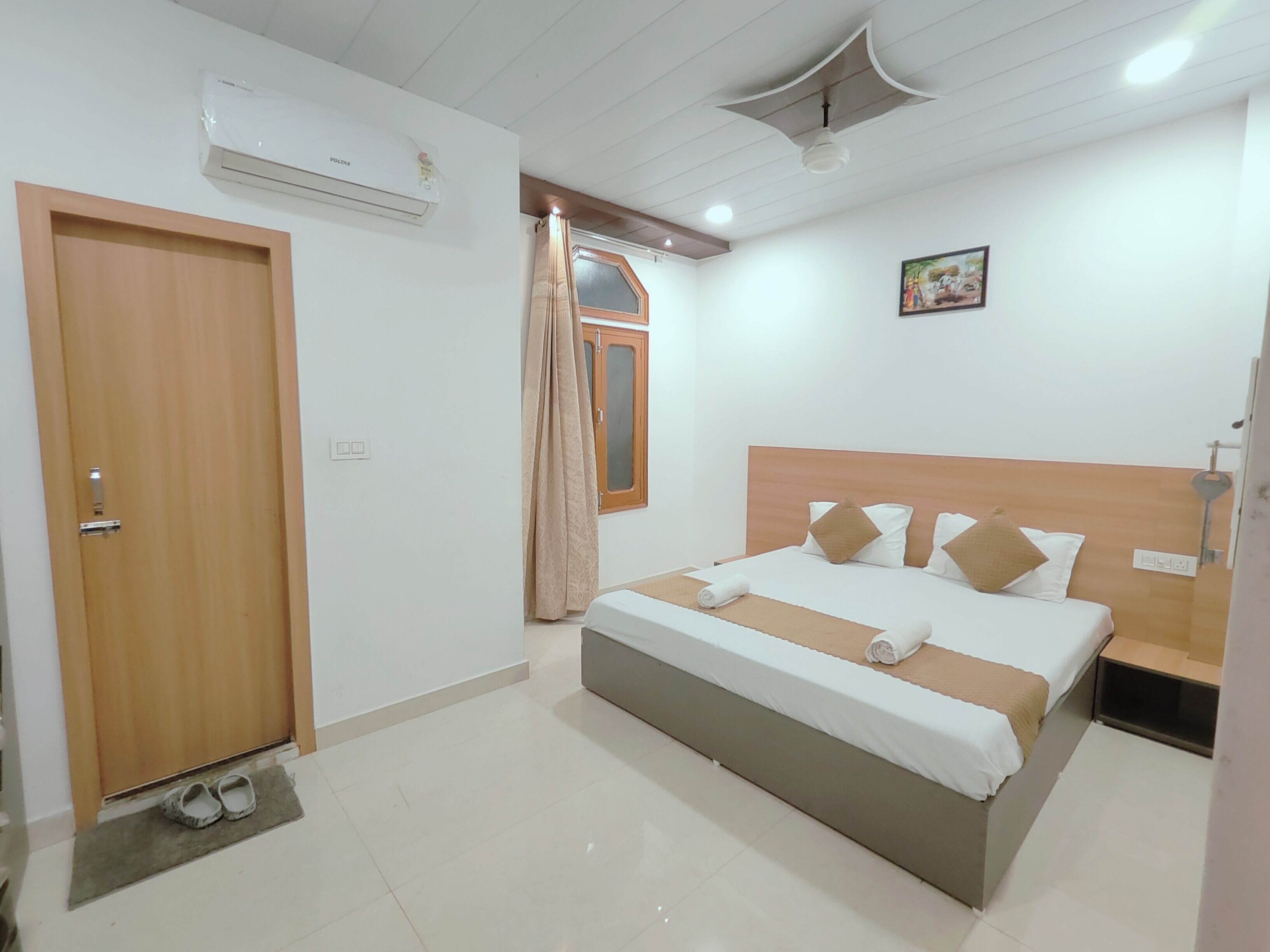 Ein Hotelzimmer mit Bett, Tür, Klimaanlage, Fenster mit Vorhängen und Deckenventilator.