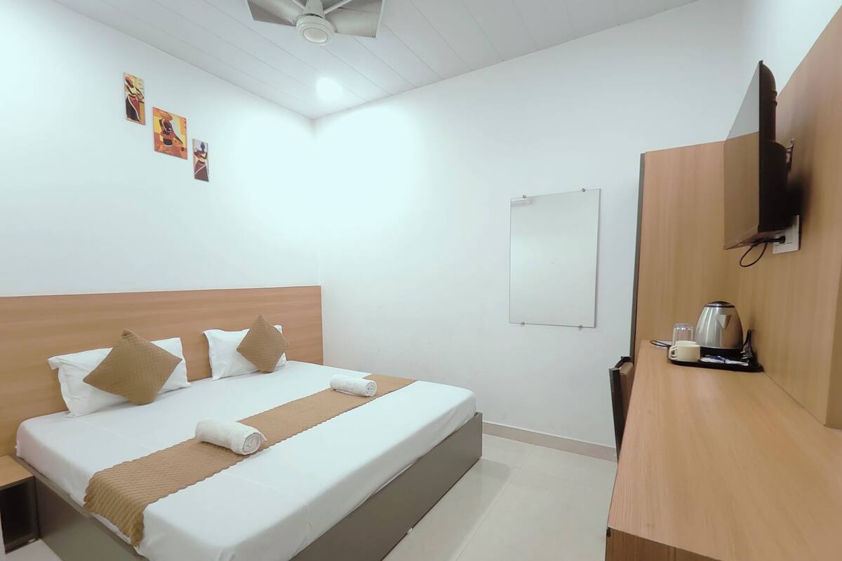 Hotelkamer met een bed, nachtkastje met koffiezetapparaat, wandtelevisie en kunst aan de muur.