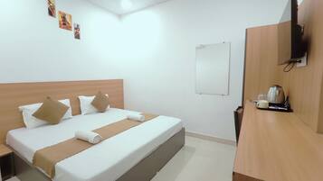 A hotel room with a bed, a bedside table with a coffee maker, a wall-mounted TV, and artwork on the wall.