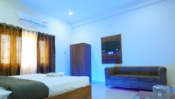 A bedroom with a bed, a wooden wardrobe, a TV mounted on the wall, and a blue sofa. - Comfort Meets Elegance Orchha ,“Your Perfect Stay, Every Time (Orchha)