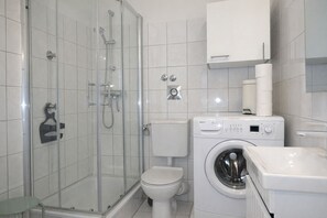 A modern bathroom with a glass-enclosed shower, a toilet, and a front-loading washing machine. - fewo1846 - Elbe27 - fewo1846 - Elbe27 - comfortable studio apartment with balcony (Flensburg)