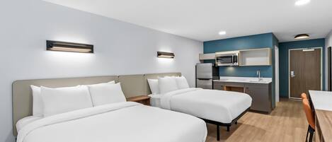 A hotel room with two beds, a kitchenette, and a dining area.