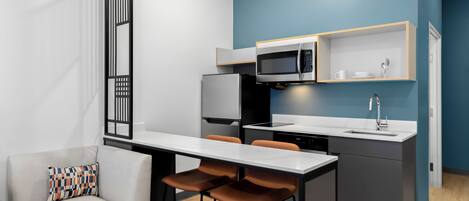 A compact kitchen with a microwave, refrigerator, and sink. There is a dining area with a table and chairs.
