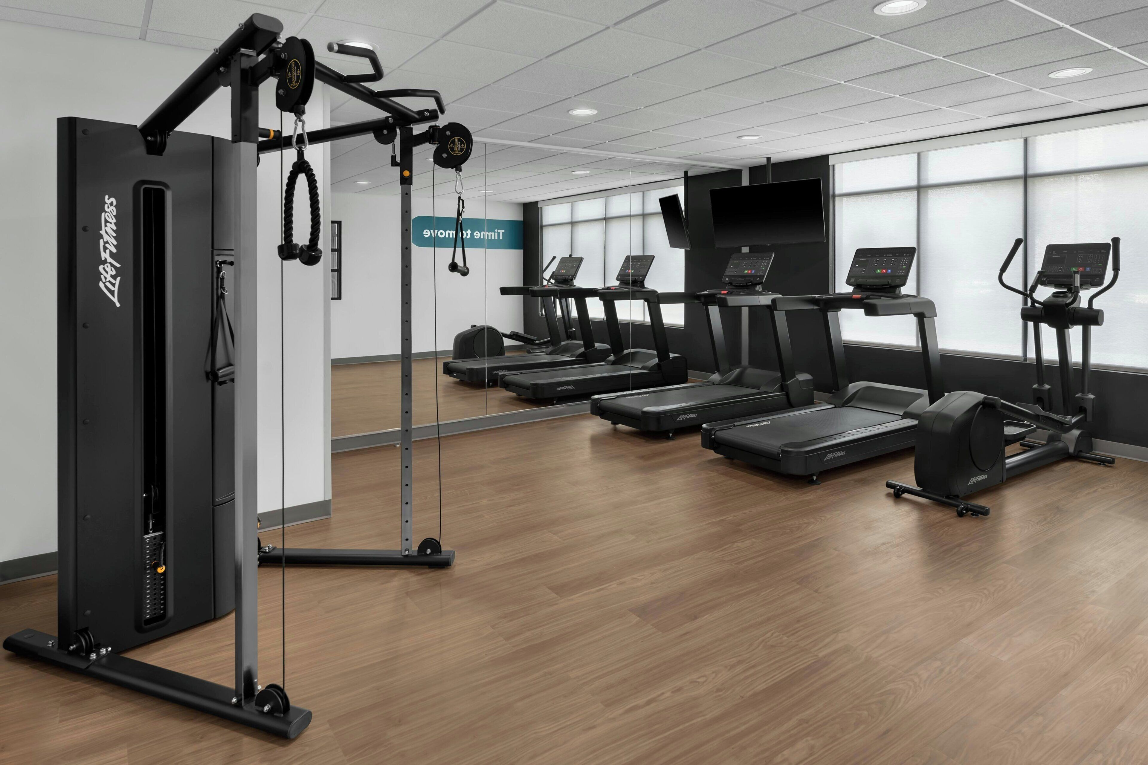 Un gimnasio con cintas de correr, una máquina de remo y una televisión montada en la pared.