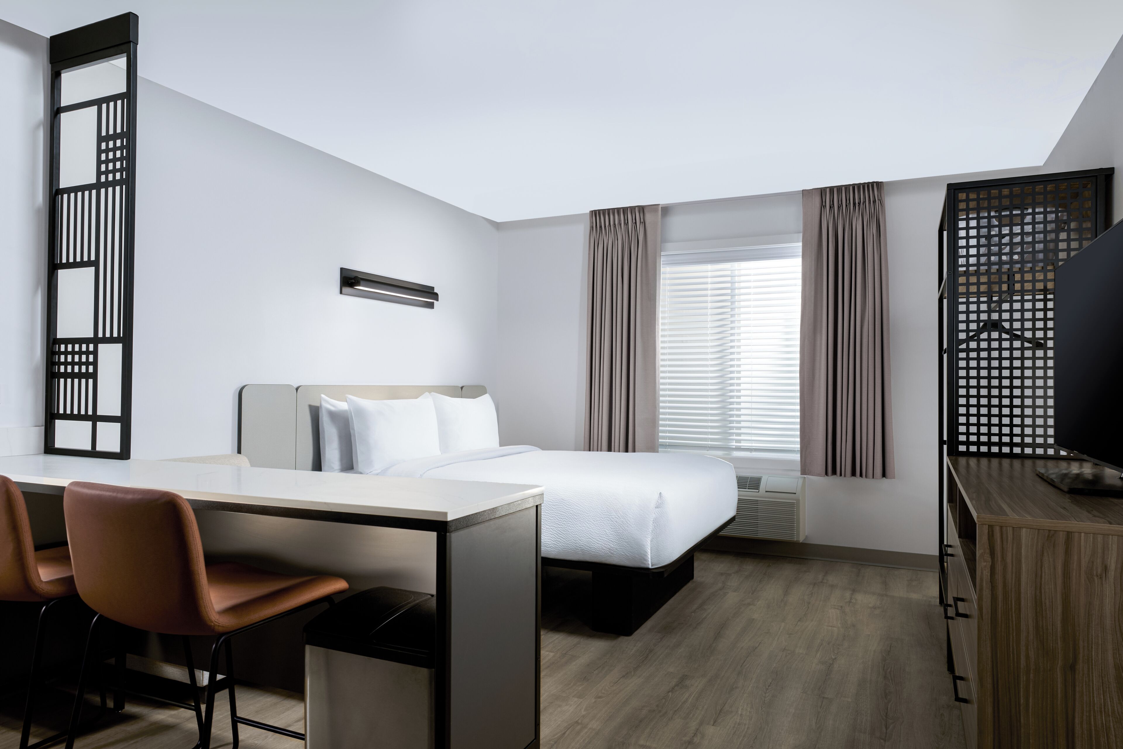 A hotel room with a bed, desk, chairs, and a TV.