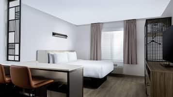 A hotel room with a bed, desk, chairs, and a TV.