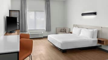 Habitación de hotel con cama, escritorio, silla, televisor y ventana con cortinas.