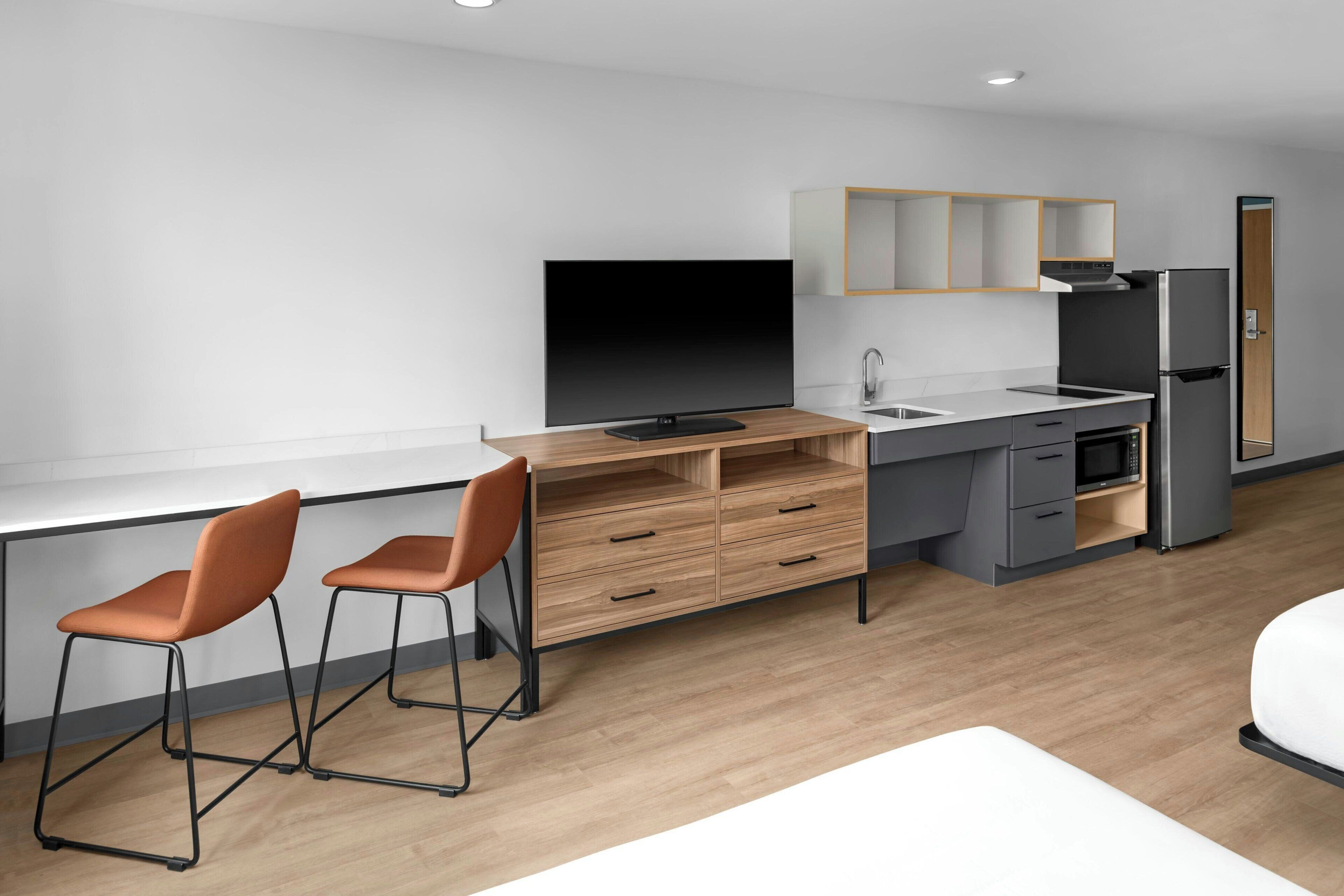 Eine moderne Küche mit Flachbildfernseher, zwei Barhocker, Kühlschrank und Mikrowelle.