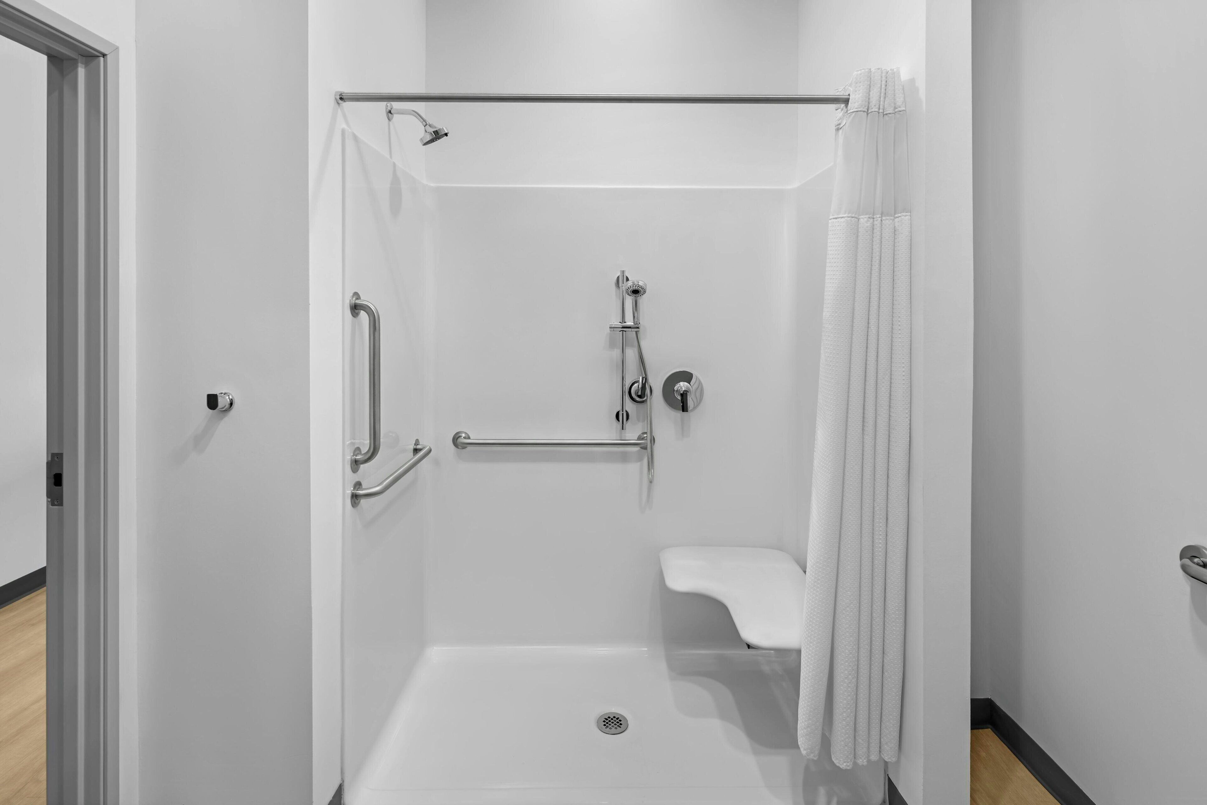 A walk-in shower with a grab bar, a handheld showerhead, and a white sink.