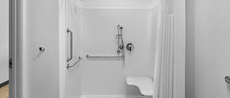 A walk-in shower with a grab bar, a handheld showerhead, and a white sink.
