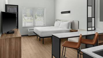 Een moderne hotelkamer met een bed, een bureau, een stoel, een televisie en een raam met jaloezieën.